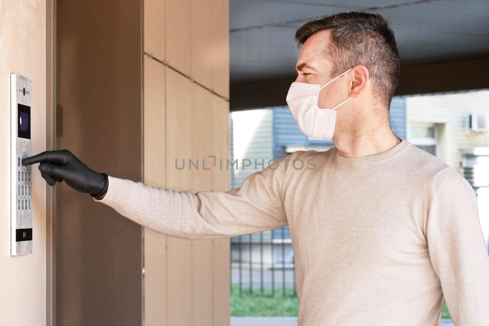 Man in face mask and gloves dials the code on the intercom and going in porch of his apartment. Pandemic covid-19 coronavirus concept