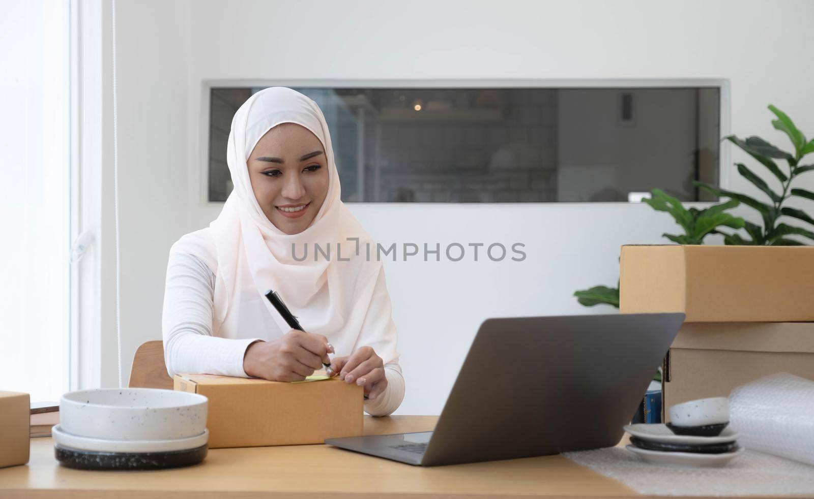 Attractive muslim female entrepreneur, e-commerce business owner packing preparing a shipping box in her office..