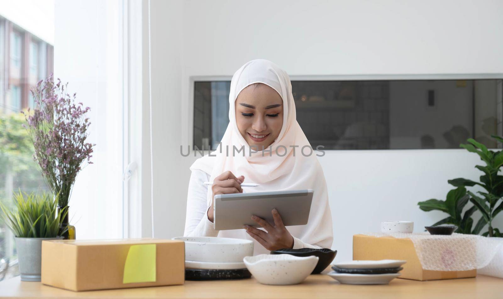 Attractive muslim female entrepreneur, e-commerce business owner packing preparing a shipping box in her office. by wichayada