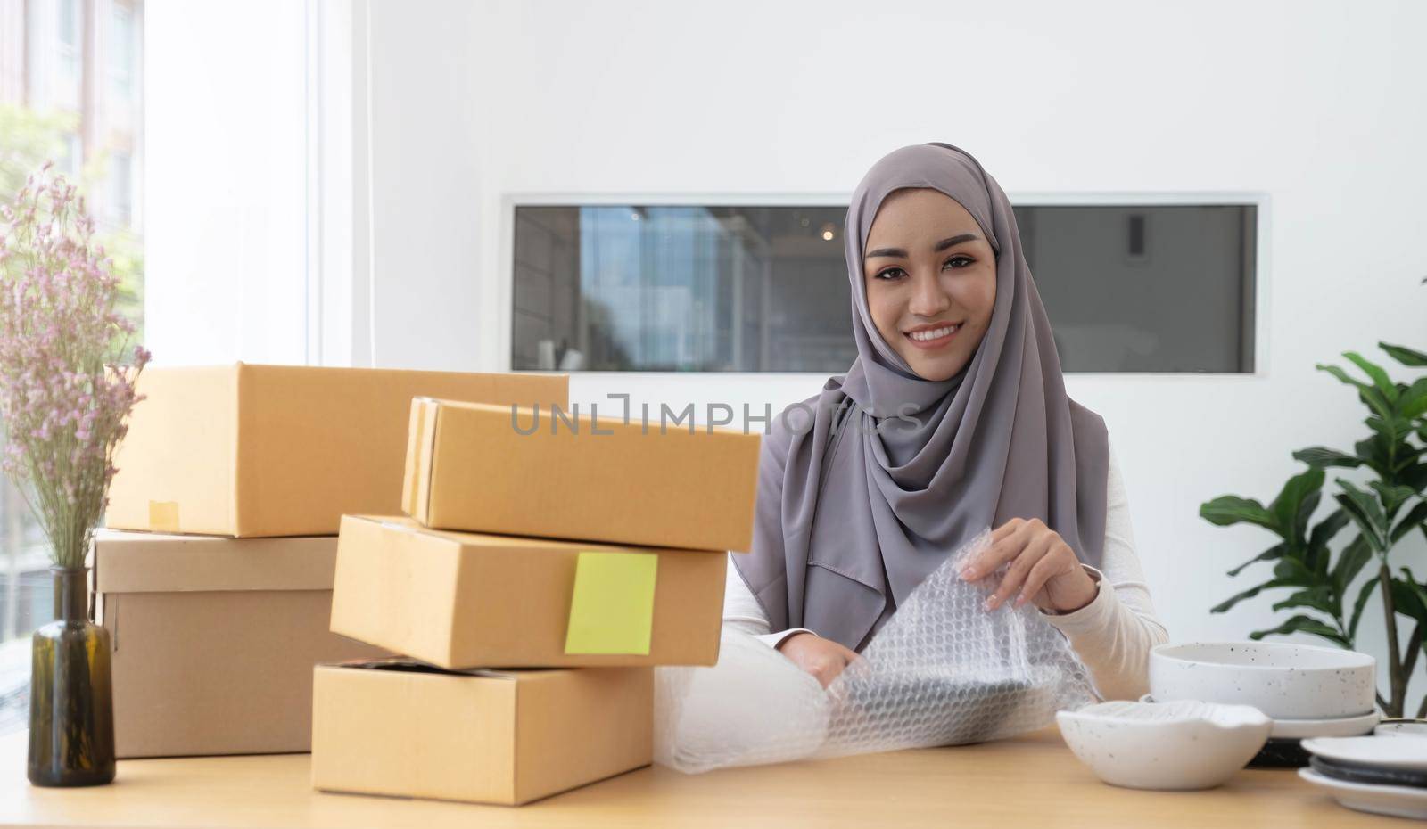 Muslim Business owner woman working online shopping prepare product packaging process at the office, young entrepreneur concept. by wichayada