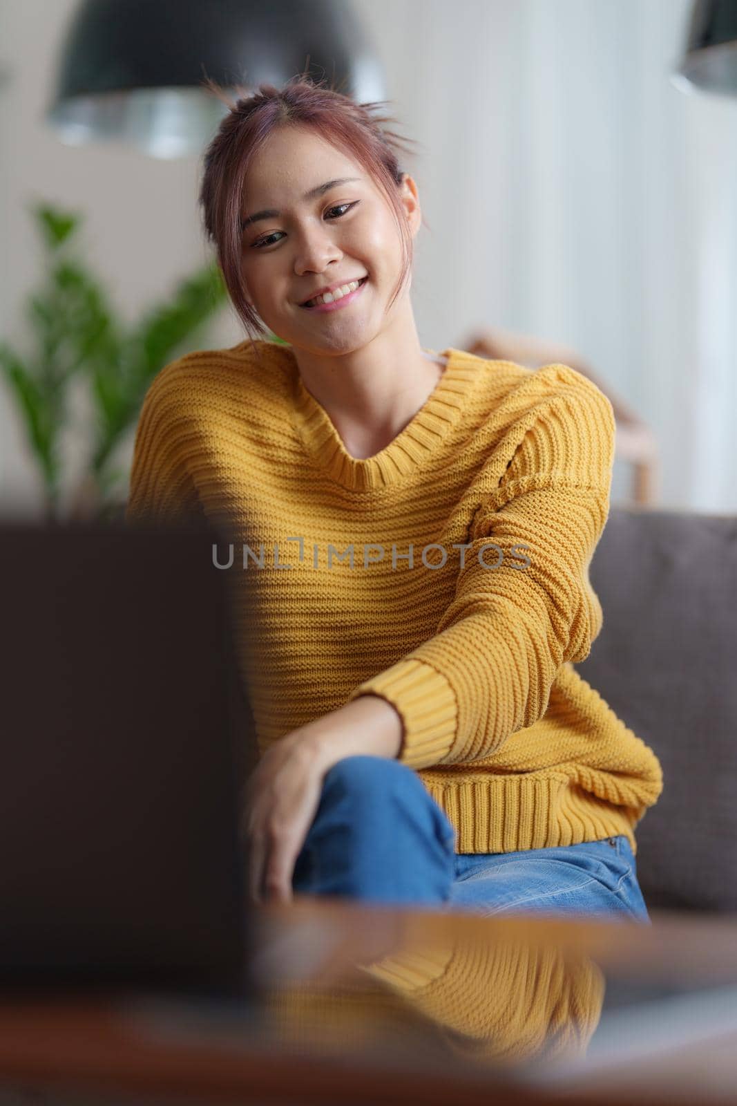 Portrait of happy asian beautiful girl making video calling with laptop and waving on phone screen at home. job interview remotely concept. by itchaznong