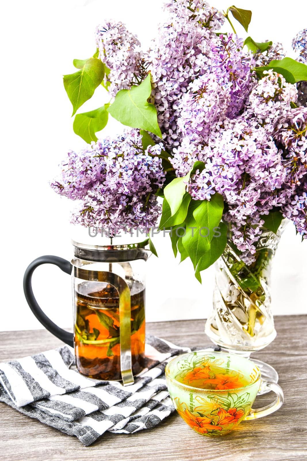 herbal tea cup and teapot and Violet lilac flowers bouquet in glass vase, Kitchen interior decorations. Mother's day congratulation by anna_stasiia