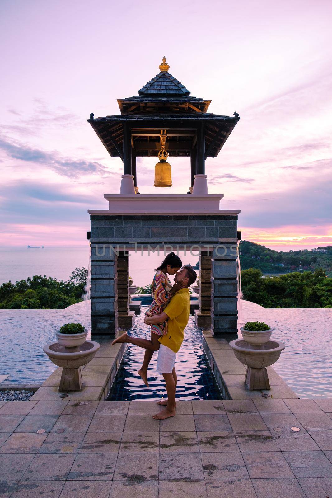 a young couple of men and women at a swimming pool during a vacation on a tropical island. man and woman in infinity pool during sunset. luxury vacation in Thailand pool of a luxury pool villa