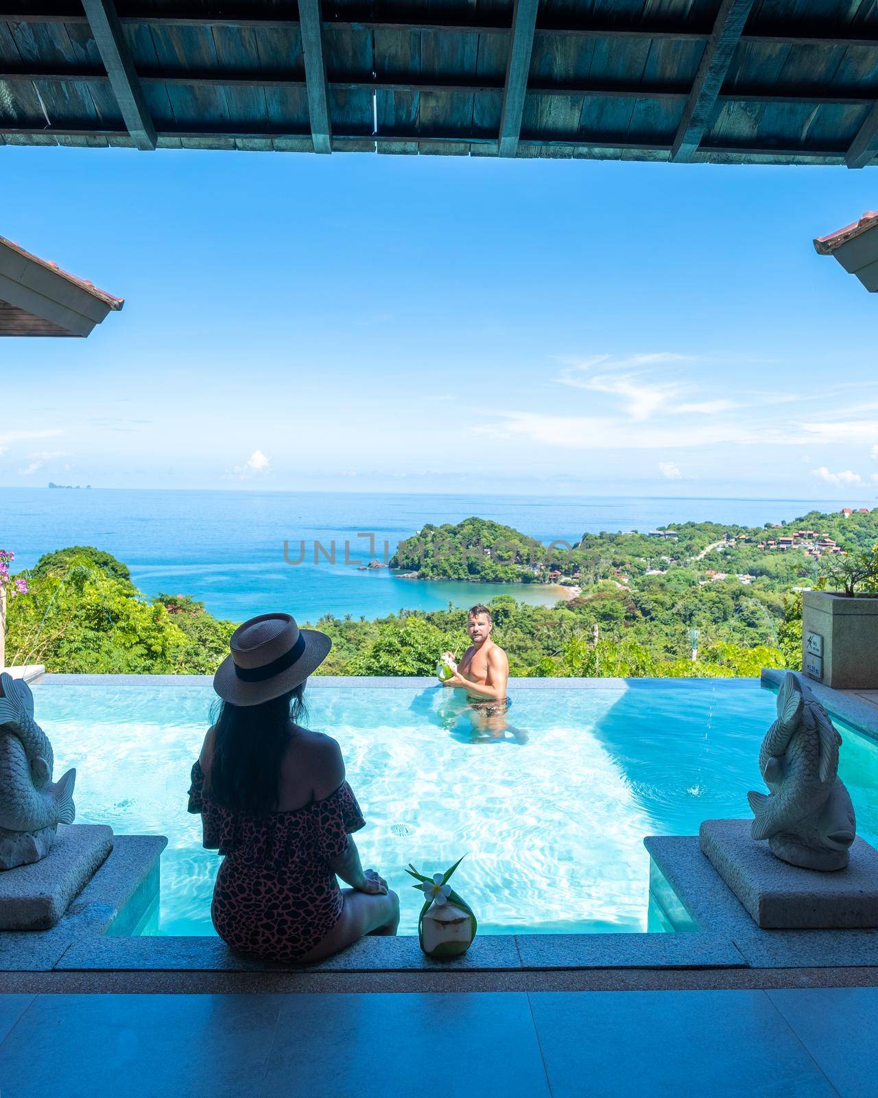 a young couple of men and women at a swimming pool during a vacation on a tropical island. man and woman in infinity pool during sunset. luxury vacation in Thailand pool of a luxury pool villa