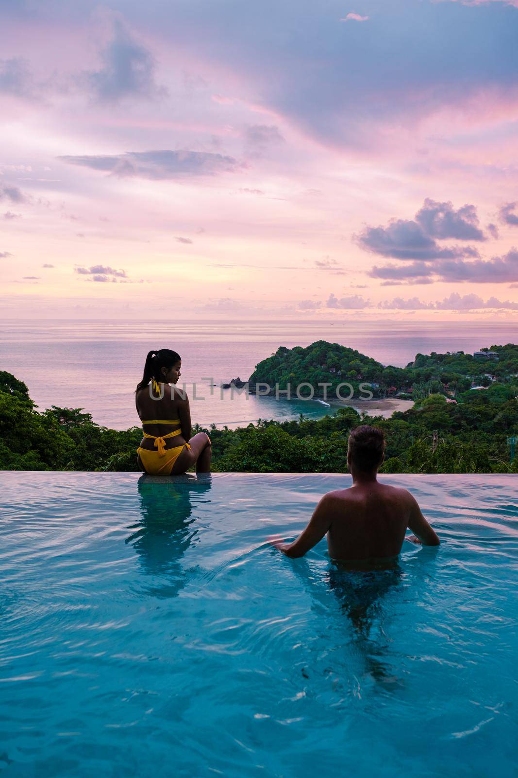 a young couple of men and women at a swimming pool during a vacation on a tropical island. man and woman in infinity pool during sunset. luxury vacation in Thailand pool of a luxury pool villa