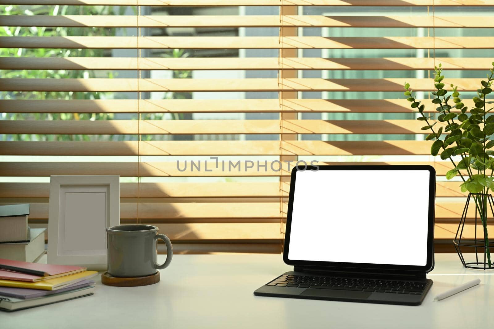 Digital tablet with wireless keyboard, coffee cup, books and picture frame on white table by prathanchorruangsak
