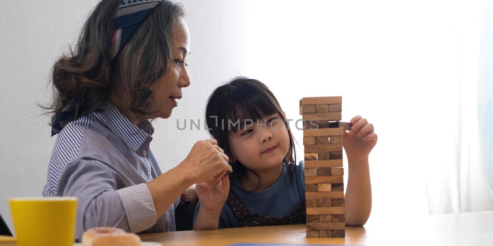 Little girl with her grandma playing jenga game at home.