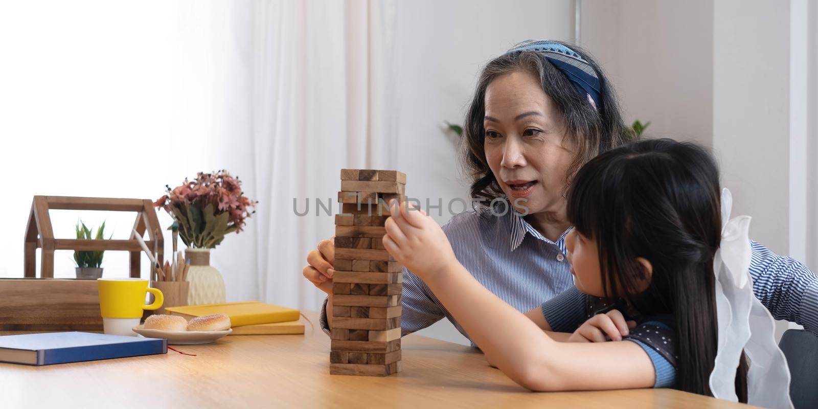 Little girl with her grandma playing jenga game at home by wichayada