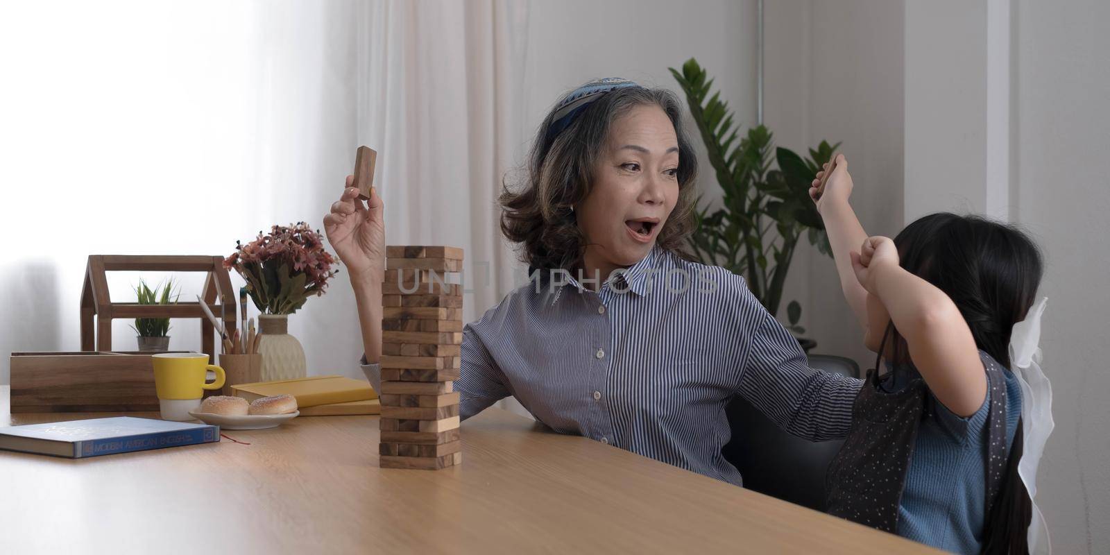 Happy moments of Asian grandmother with her granddaughter playing jenga constructor. Leisure activities for children at home. by wichayada