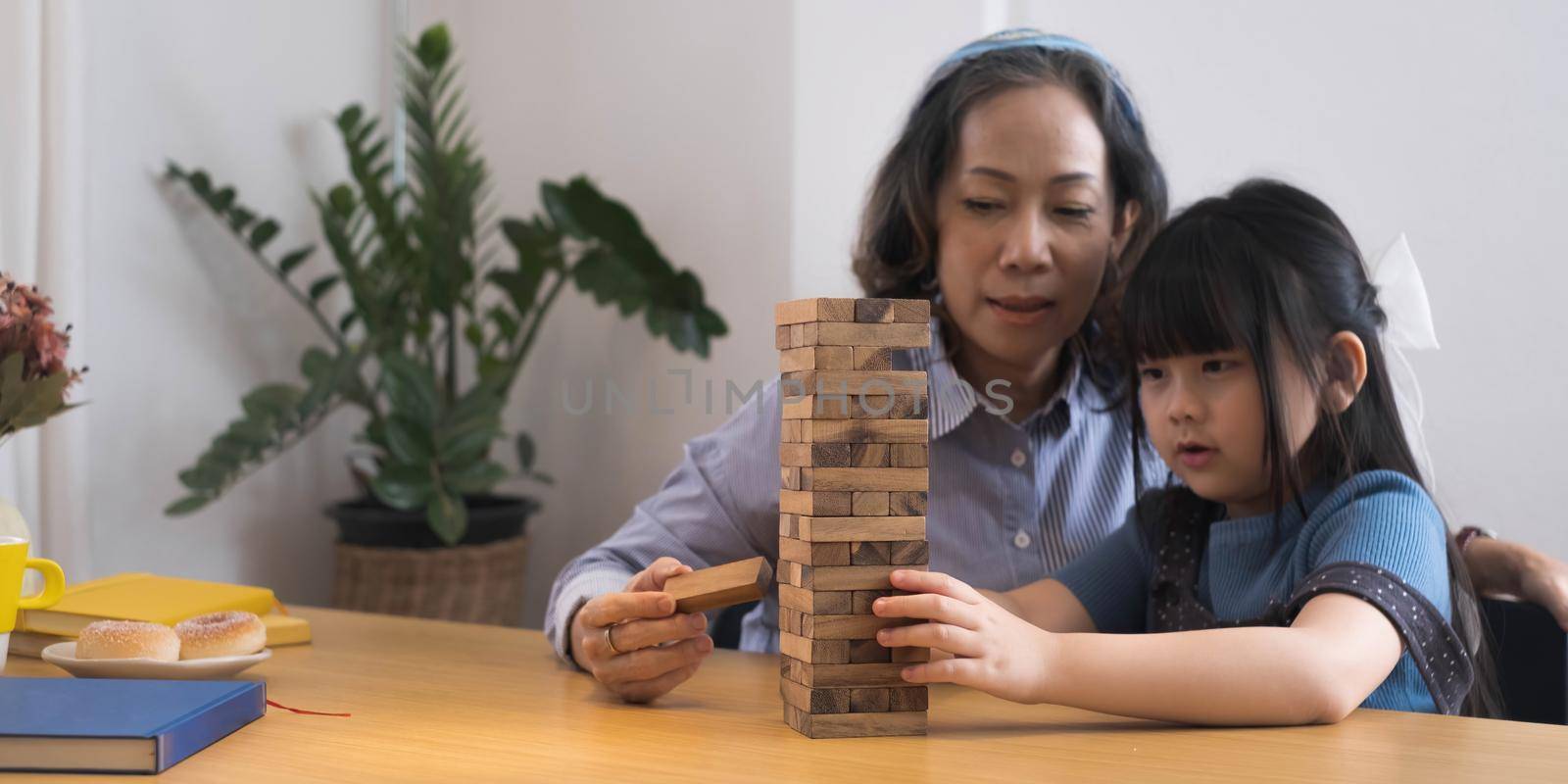 Happy moments of Asian grandmother with her granddaughter playing jenga constructor. Leisure activities for children at home. by wichayada