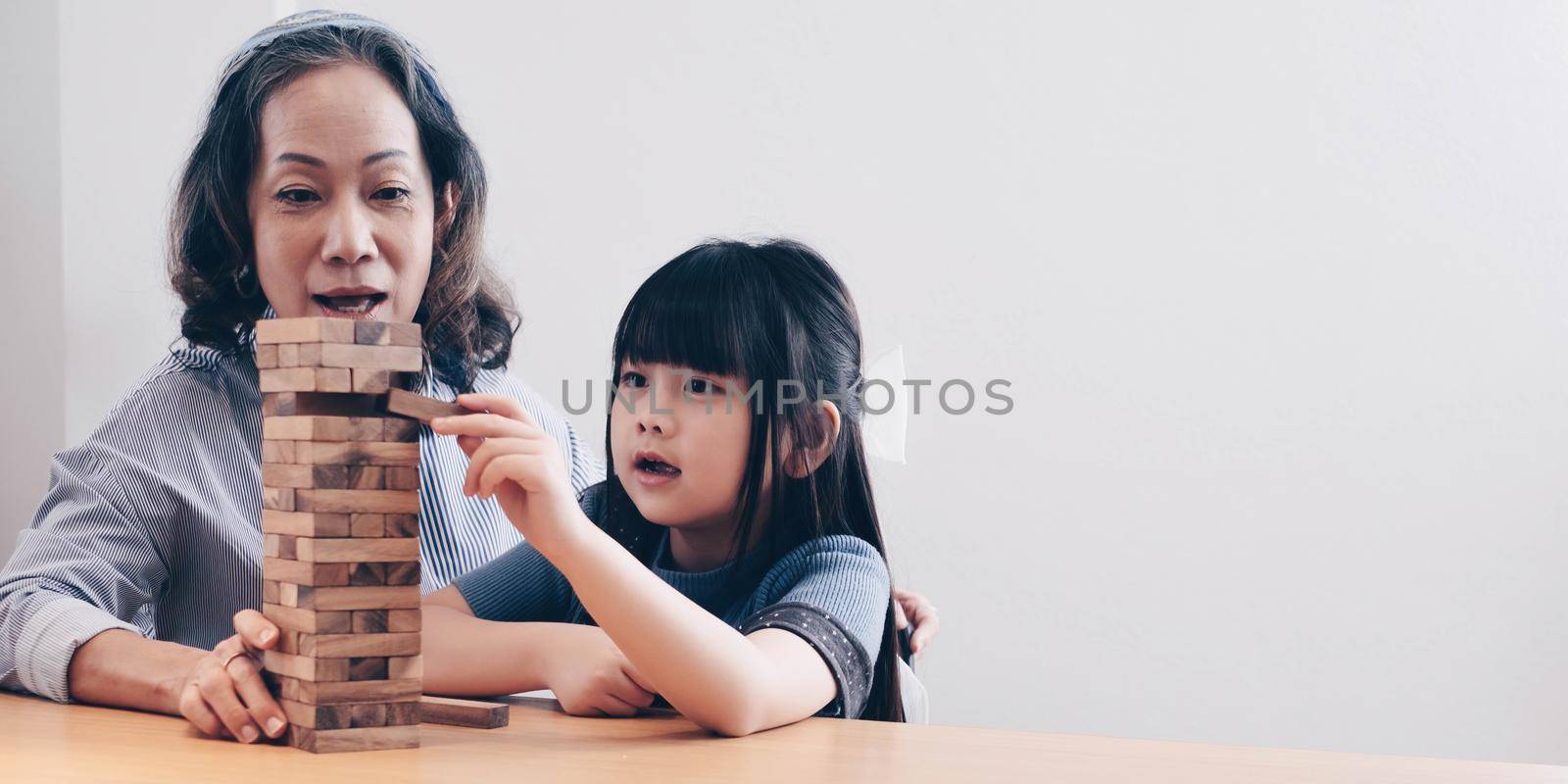 Little girl with her grandma playing jenga game at home by wichayada