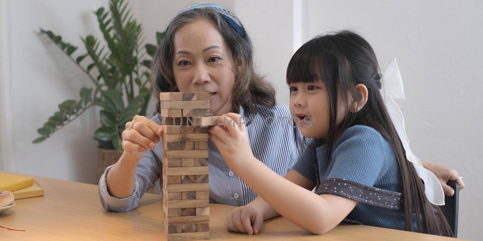 Little girl with her grandma playing jenga game at home.