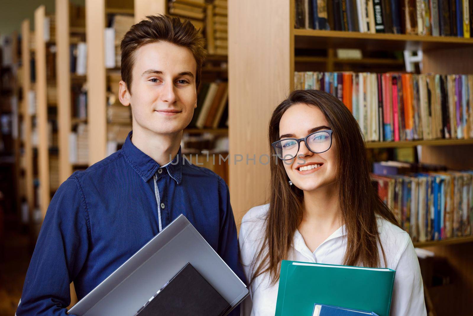 Students at the library in front of shelves of books, studying together, smiling to the camera, eager to study