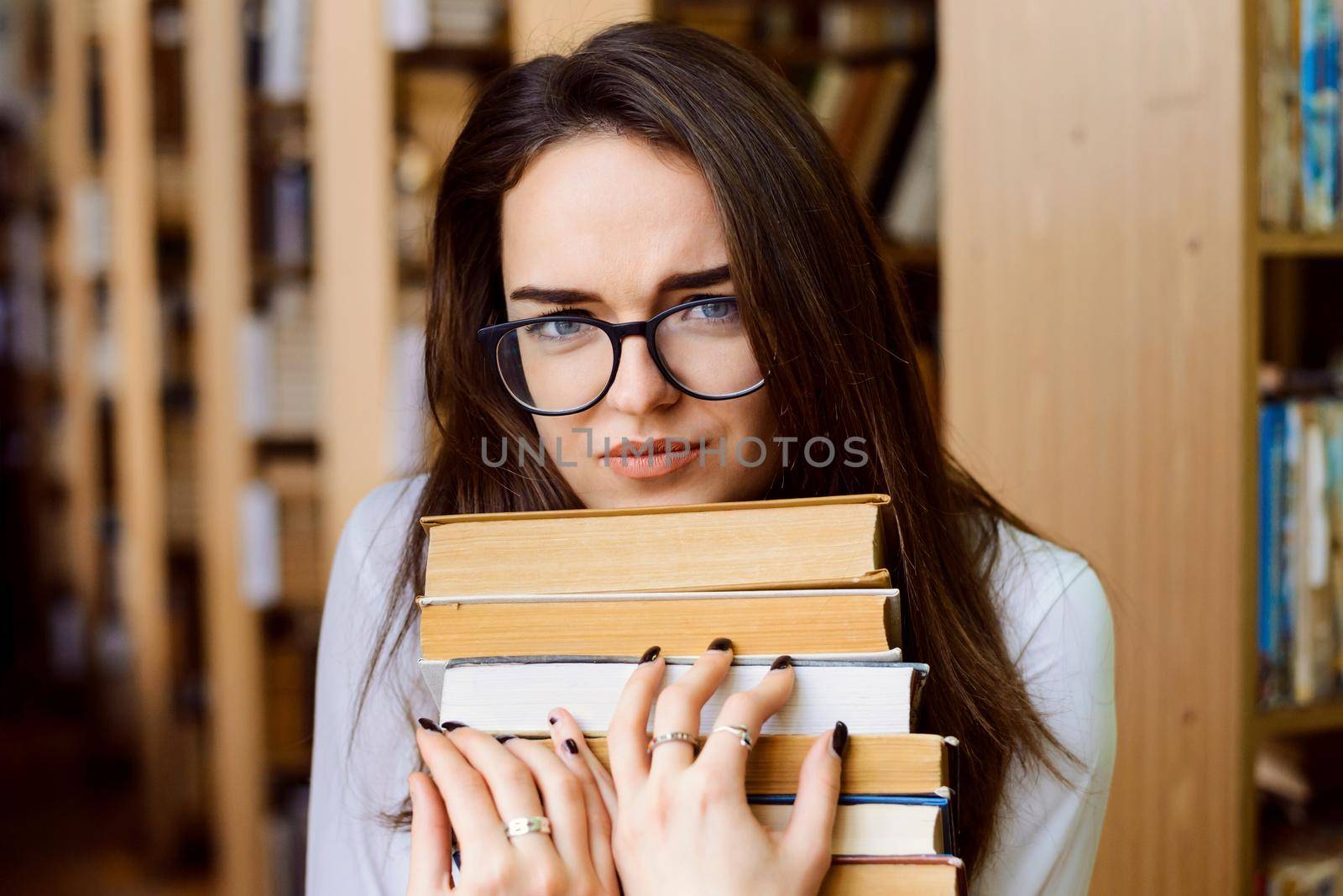 Tired female student in library with a lot of books preparing for exams