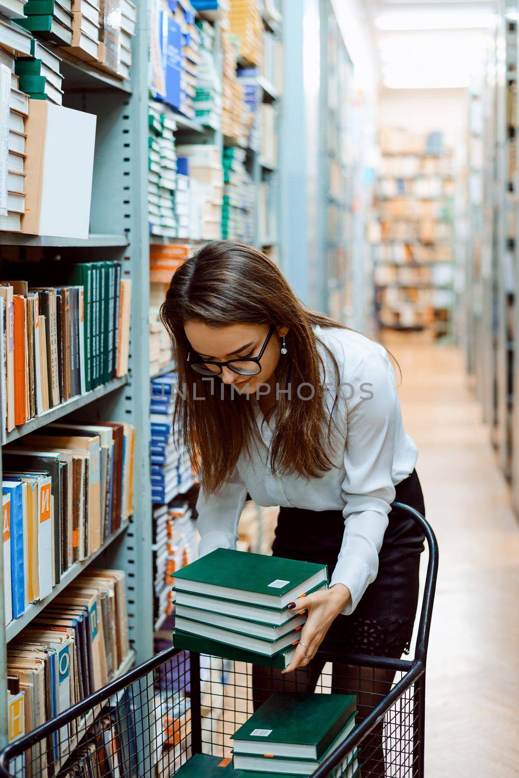 Librarian puts piles of new books to the shelves of the library, doing her job