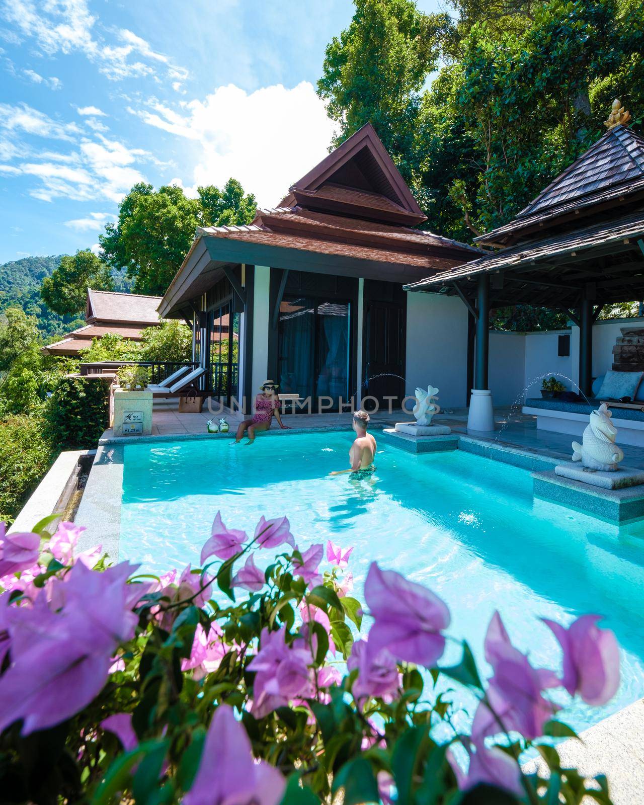 a young couple of men and women at a swimming pool during a vacation on a tropical island. man and woman in infinity pool during sunset. luxury vacation in Thailand pool of a luxury pool villa