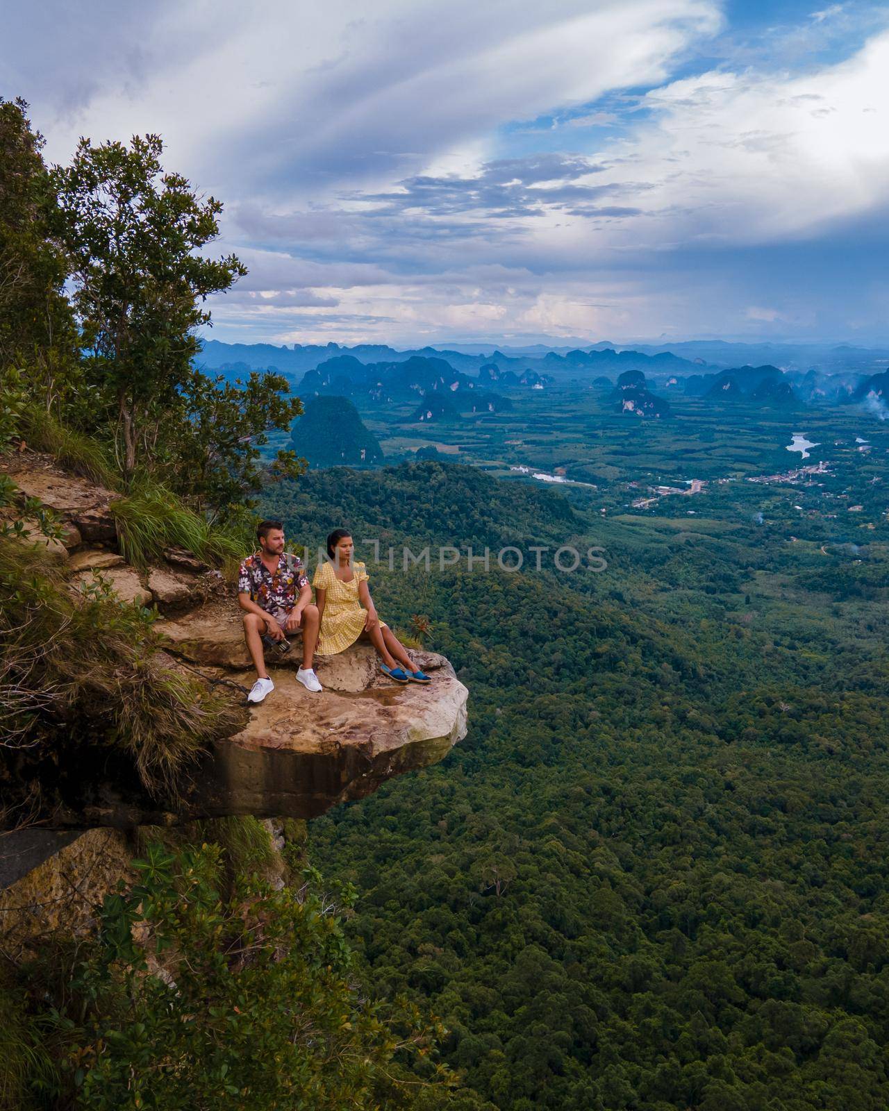 Dragon Crest mountain Krabi Thailand, a Young traveler sits on a rock that overhangs the abyss, with a beautiful landscape. Dragon Crest or Khuan Sai at Khao Ngon Nak Nature Trail in Krabi, Thailand