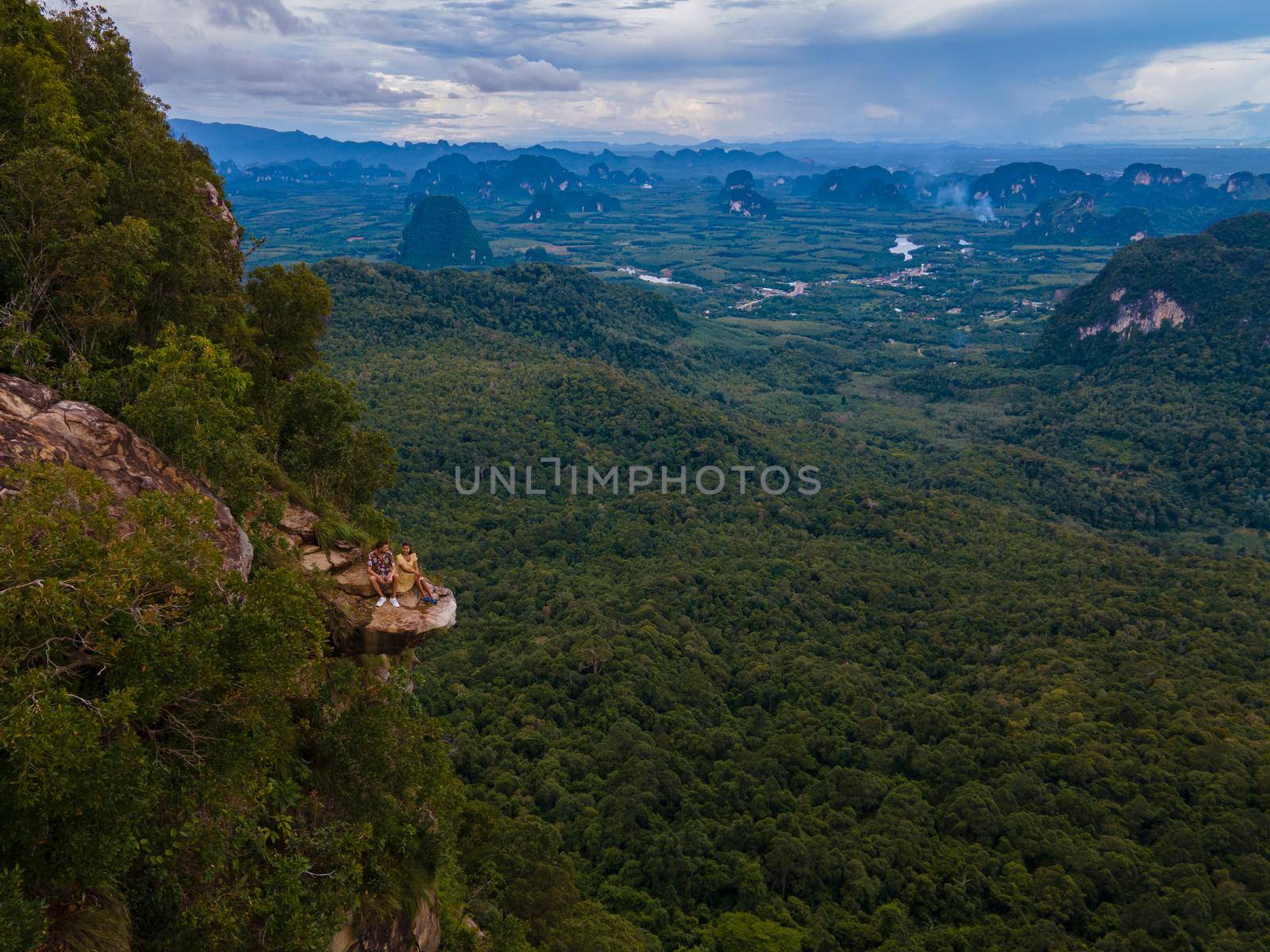 Dragon Crest mountain Krabi Thailand, a Young traveler sits on a rock that overhangs the abyss, with a beautiful landscape. Dragon Crest or Khuan Sai at Khao Ngon Nak Nature Trail in Krabi, Thailand