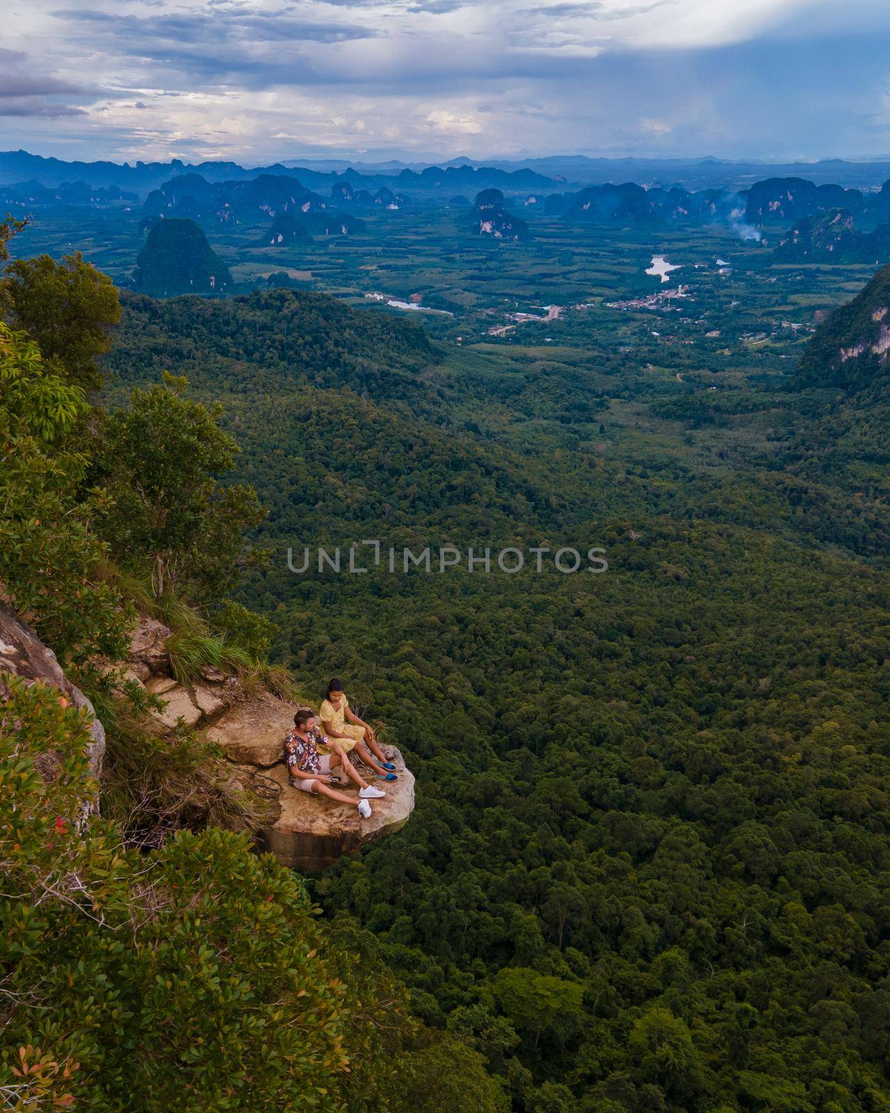 Dragon Crest mountain Krabi Thailand, a Young traveler sits on a rock that overhangs the abyss, with a beautiful landscape. Dragon Crest or Khuan Sai at Khao Ngon Nak Nature Trail in Krabi, Thailand