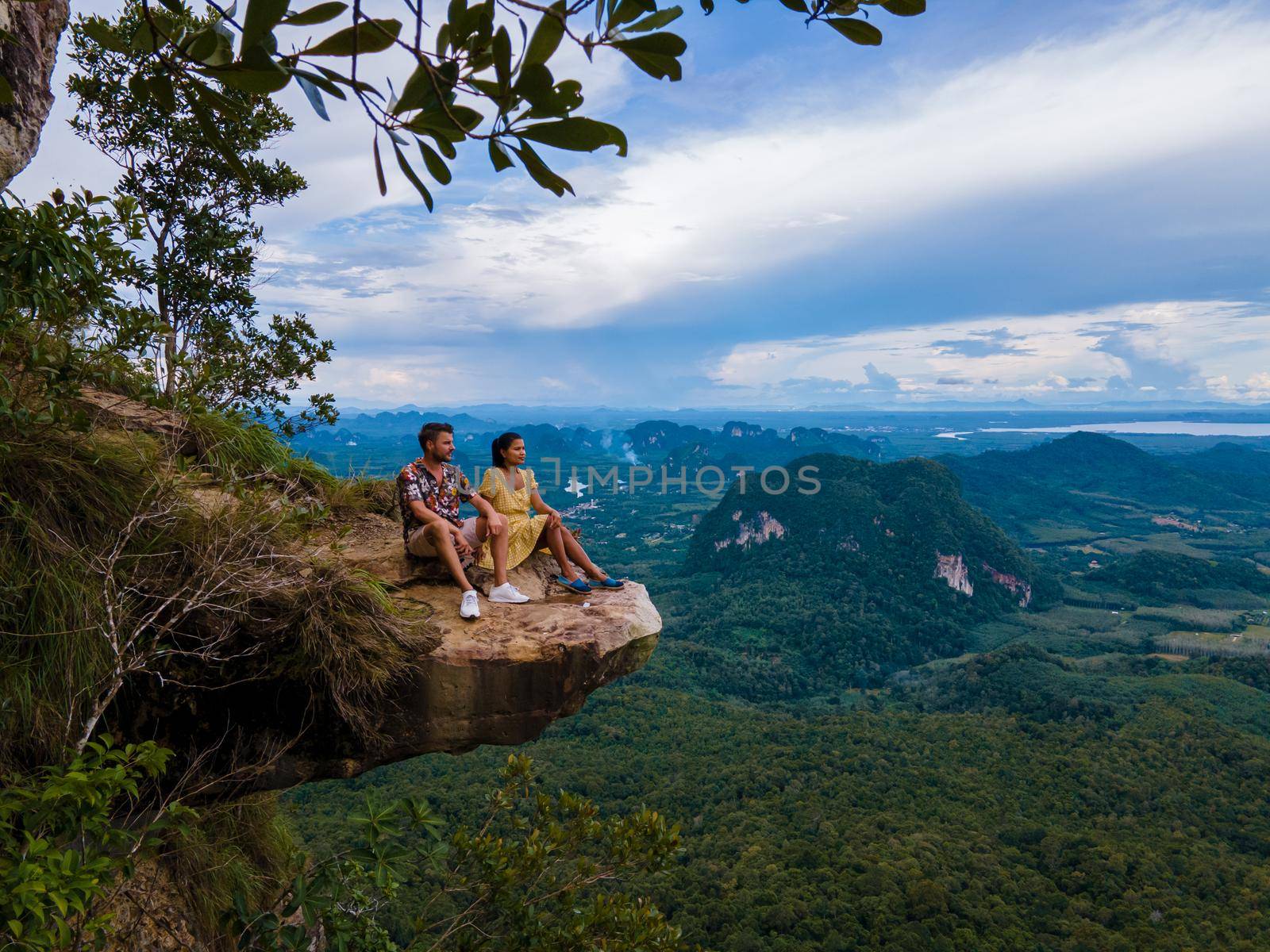 Dragon Crest mountain Krabi Thailand, a Young traveler sits on a rock that overhangs the abyss, with a beautiful landscape. Dragon Crest or Khuan Sai at Khao Ngon Nak Nature Trail in Krabi, Thailand