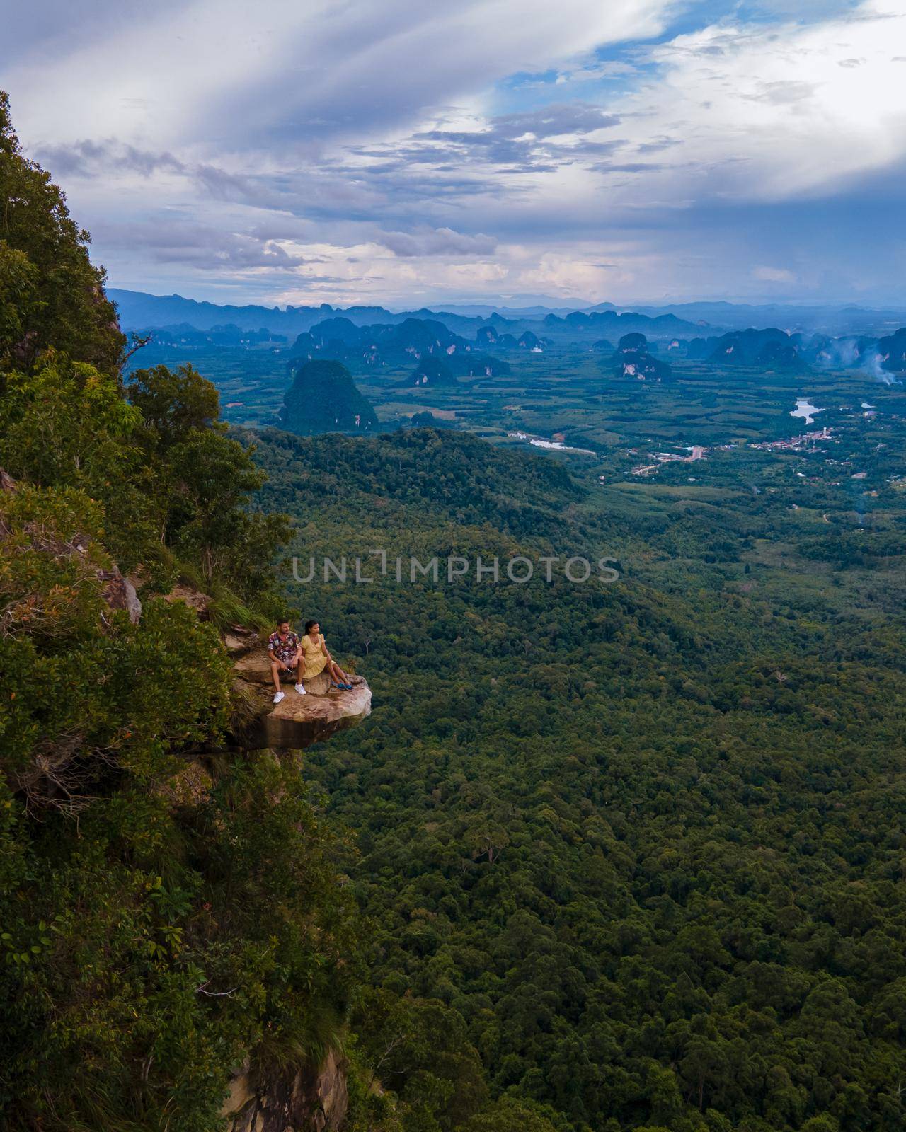 Dragon Crest mountain Krabi Thailand, a Young traveler sits on a rock that overhangs the abyss, with a beautiful landscape. Dragon Crest or Khuan Sai at Khao Ngon Nak Nature Trail in Krabi, Thailand