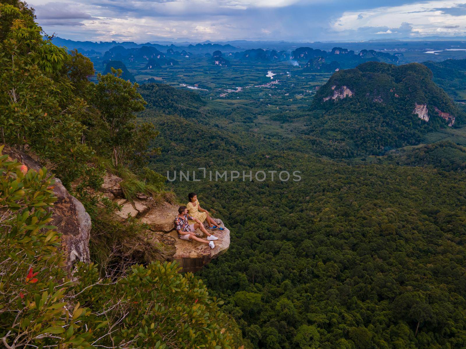 Dragon Crest mountain Krabi Thailand, a Young traveler sits on a rock that overhangs the abyss, with a beautiful landscape. Dragon Crest or Khuan Sai at Khao Ngon Nak Nature Trail in Krabi, Thailand