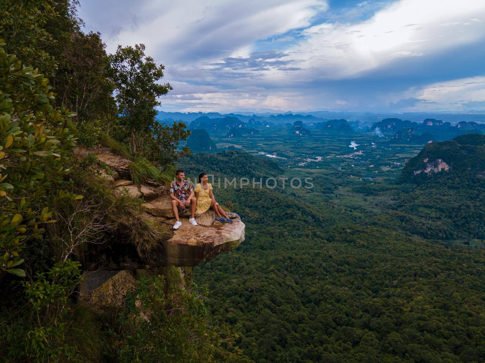 Dragon Crest mountain Krabi Thailand, a Young traveler sits on a rock that overhangs the abyss, with a beautiful landscape. Dragon Crest or Khuan Sai at Khao Ngon Nak Nature Trail in Krabi, Thailand