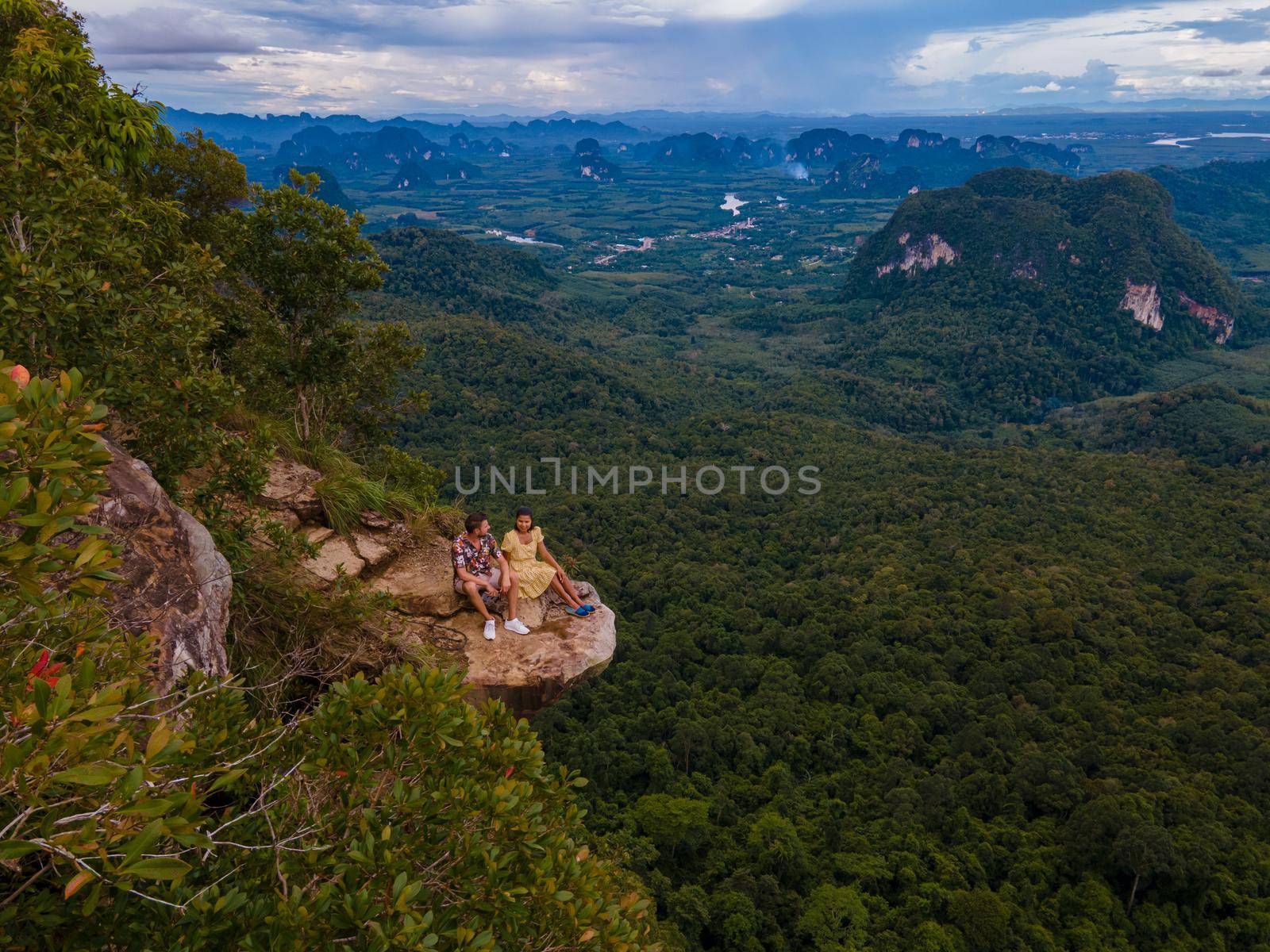 Dragon Crest mountain Krabi Thailand, a Young traveler sits on a rock that overhangs the abyss, with a beautiful landscape. Dragon Crest or Khuan Sai at Khao Ngon Nak Nature Trail in Krabi, Thailand