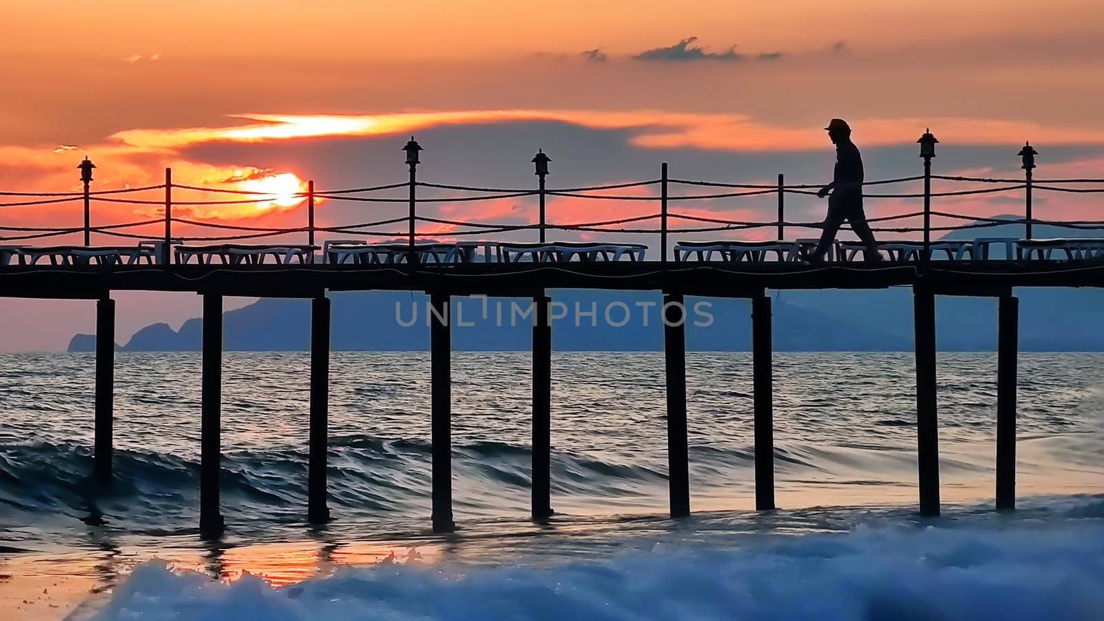 Evening seascape with beautiful sunset. Silhouette of man walking on bridge over sea, in background of sunset.