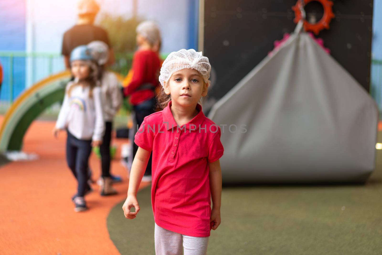 Cute little girl climber dressed protective hat before dress up helmet standing in climber centre amusement park for children. Caucasian female climber 5 years