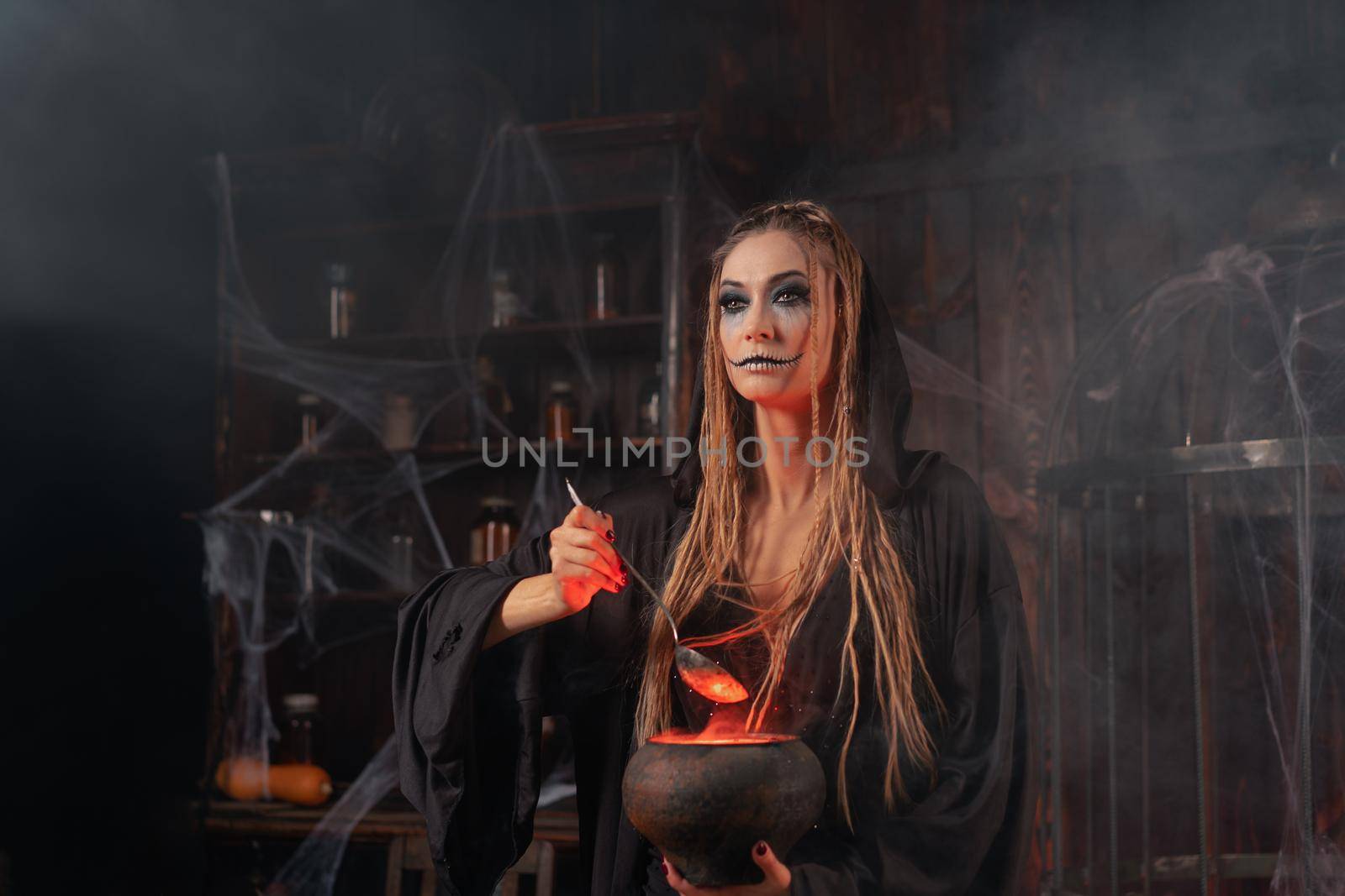 Halloween, witch use magic book and cauldron prepare poison or love potion. Black magic occult female wizard in dark room with smoke, spider web. Necromancer cooking magic potion. Close up