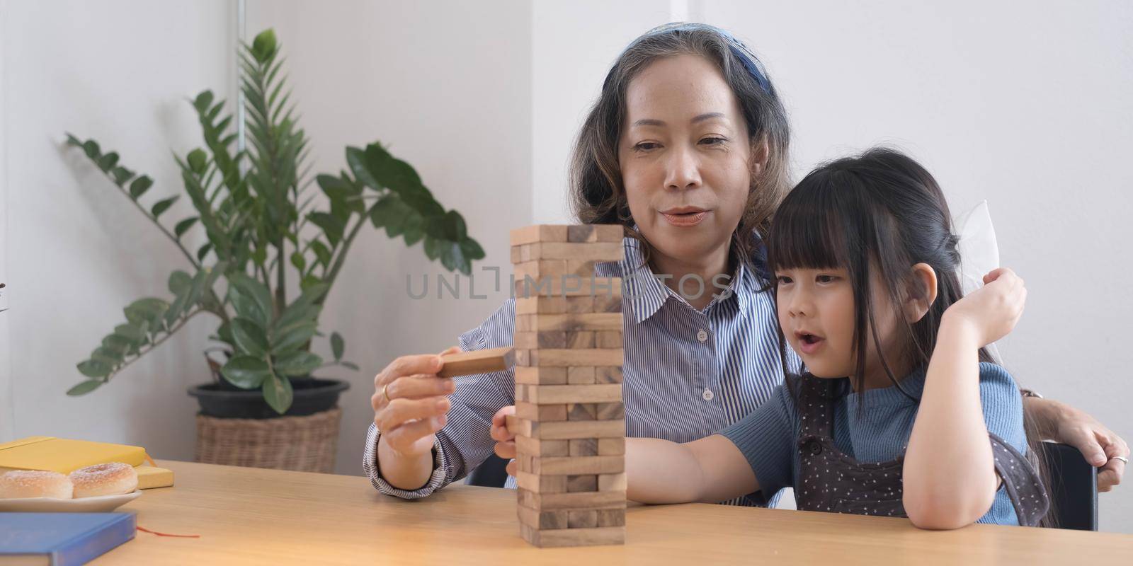 Happy moments of Asian grandmother with her granddaughter playing jenga constructor. Leisure activities for children at home..