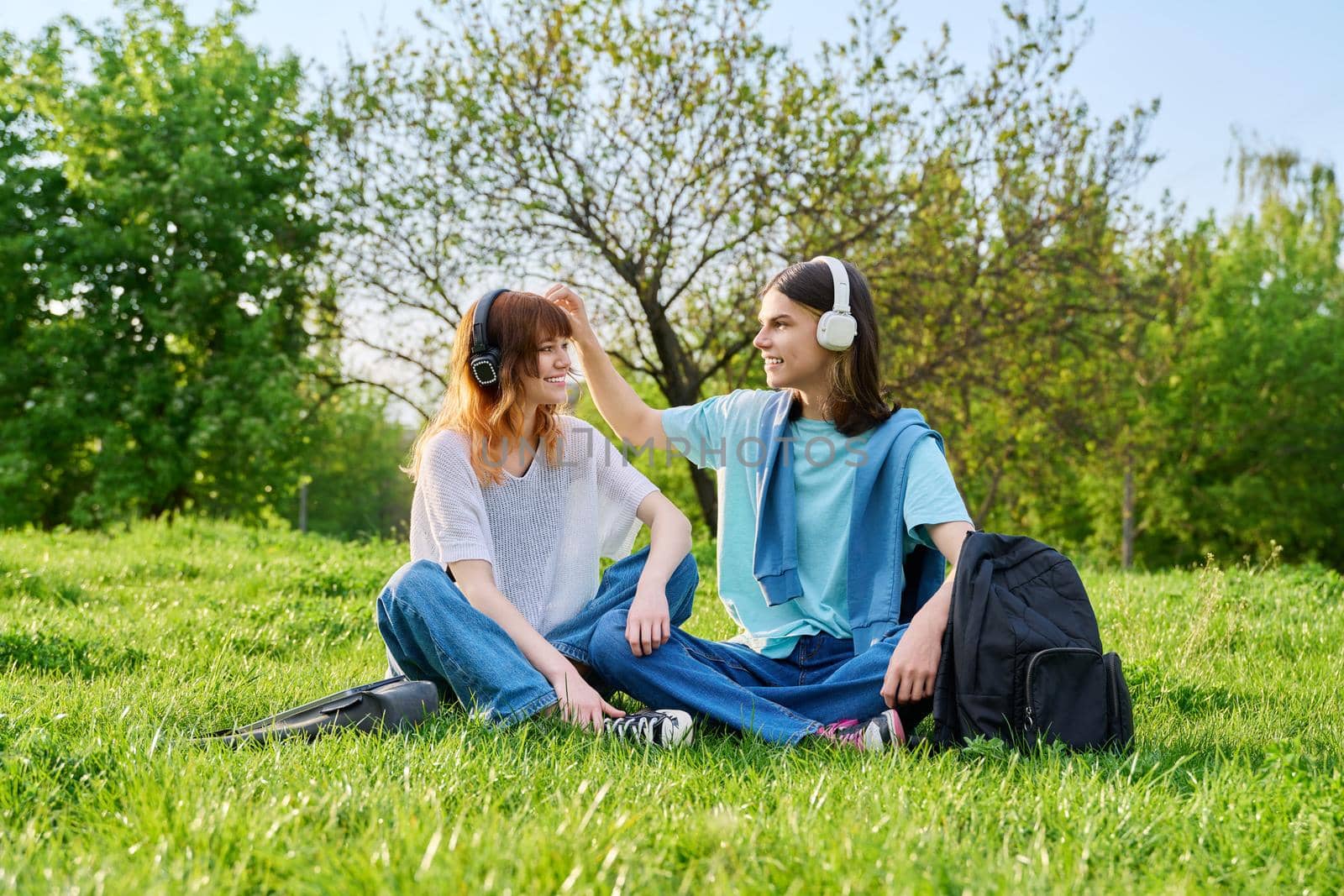 Couple of friends guy and girl 17, 18 years old sitting on grass by VH-studio