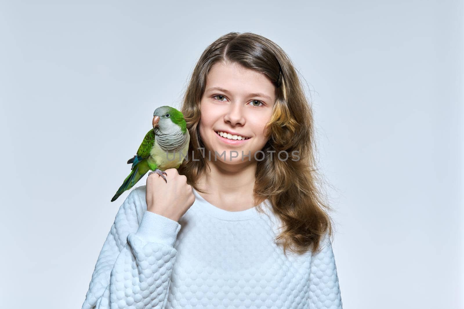 Child girl with pet green quaker parrot looking at camera on light studio background by VH-studio