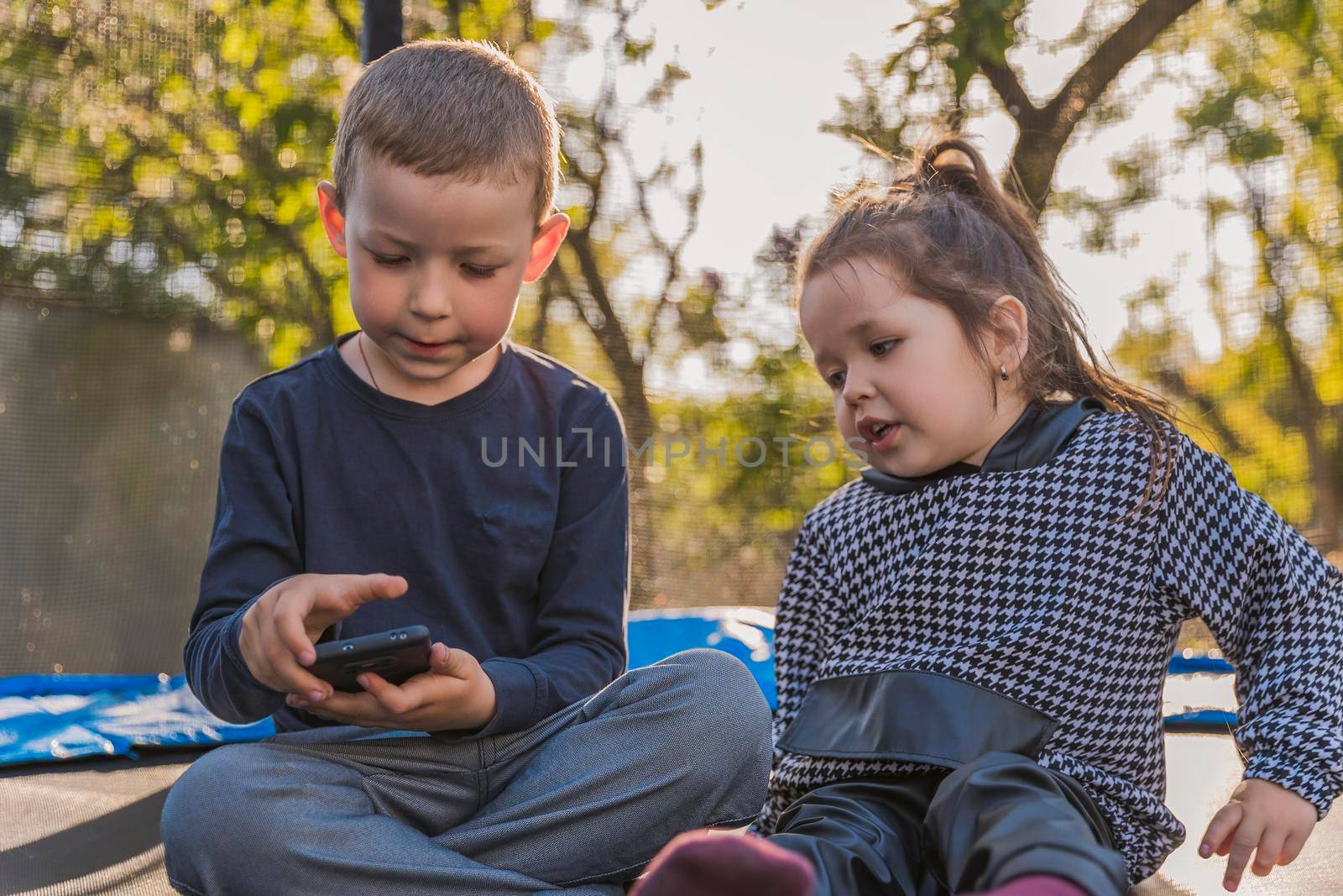 children sit on a trampoline and look at the phone