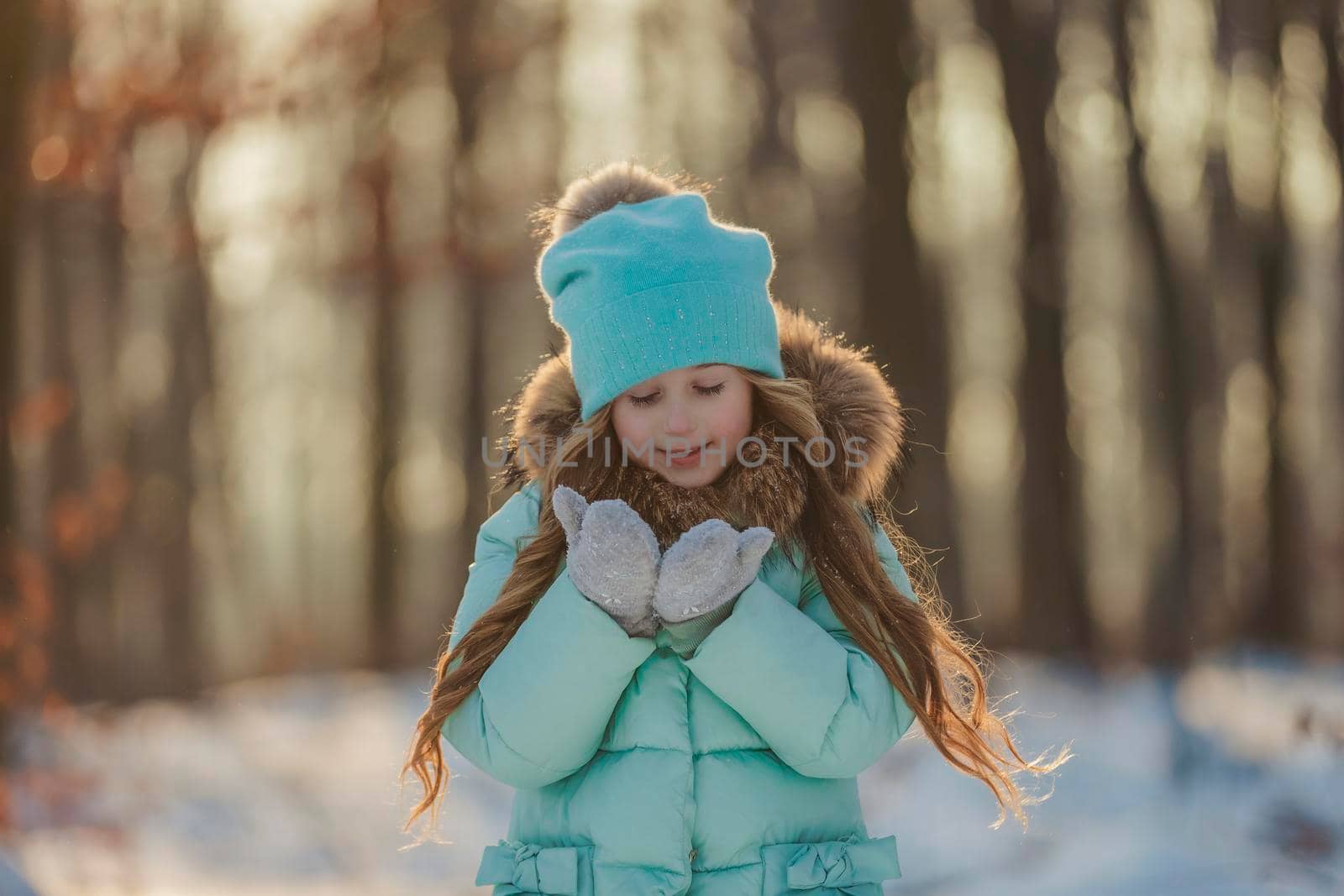 little girl blows on the snow that is on her mittens