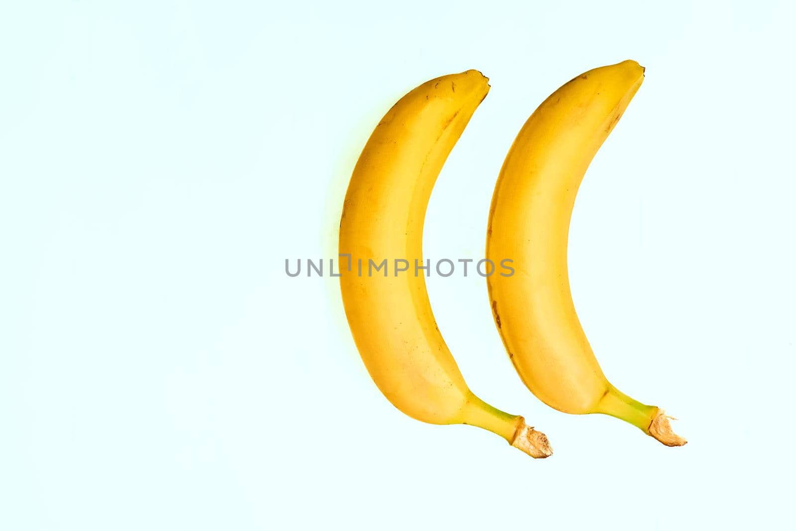 a long curved fruit which grows in clusters and has soft pulpy flesh and yellow skin when ripe.Two ripe bananas on a pale green background.