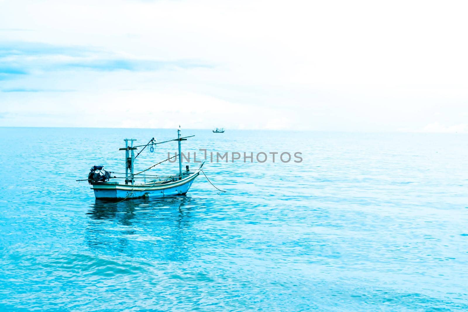 Small fishing boat floating in blue sea with blue sky Thailand.