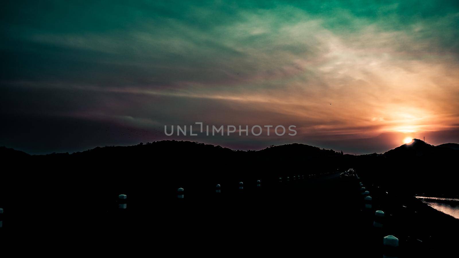 Sunset landscape with orange sky, silhouettes of mountains, hills and trees and lake