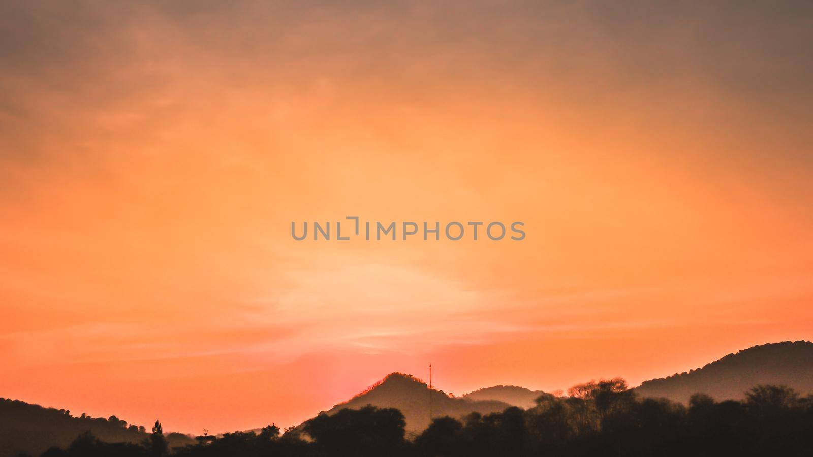 Sunset landscape with orange sky, silhouettes of mountains, hills and trees and lake