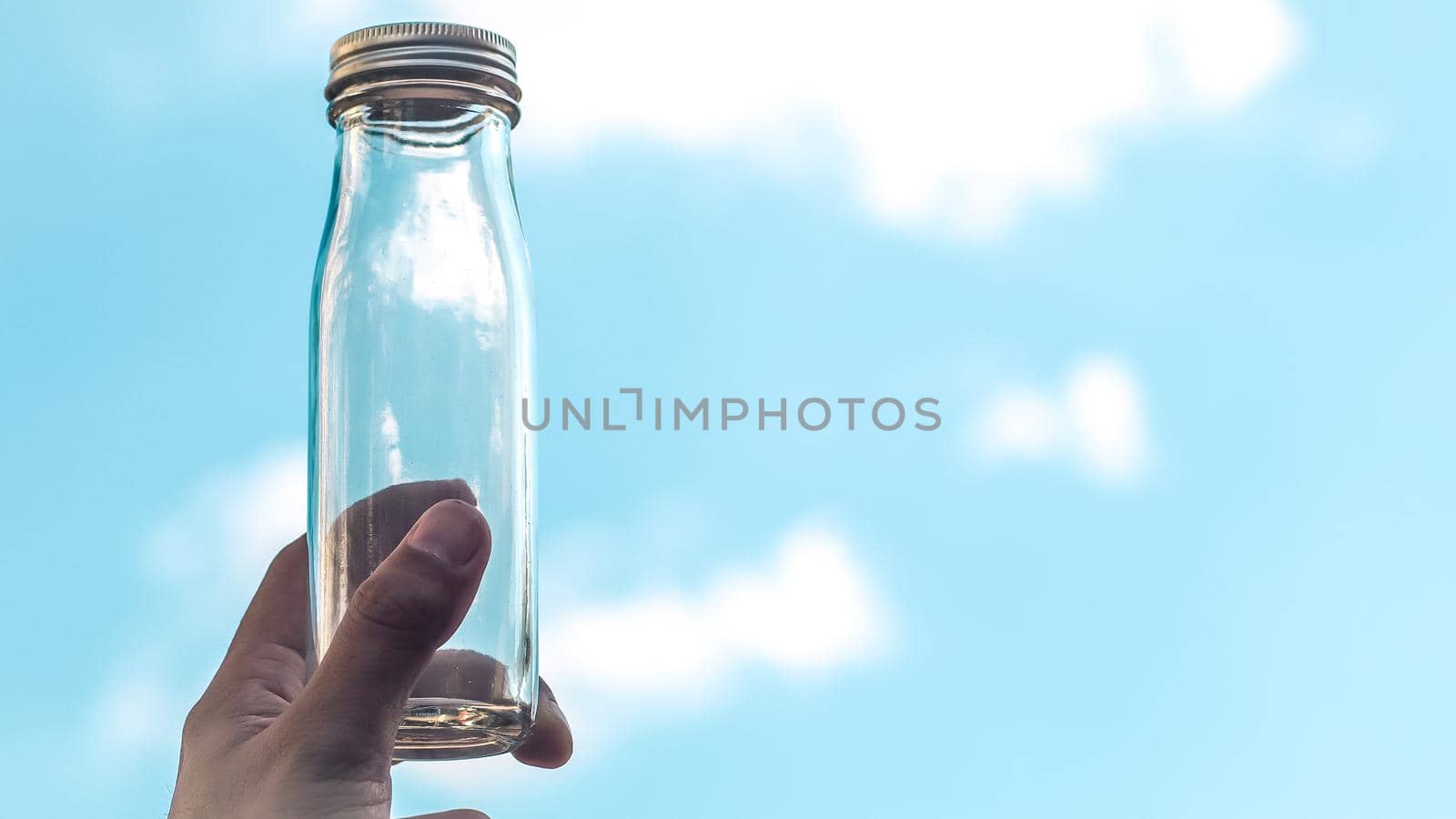 Male Hand hold transparent glass bottle. Empty bottle fill with blue sky. Against blue sky. Empty copy space. Clean air environment nature for life concept idea background