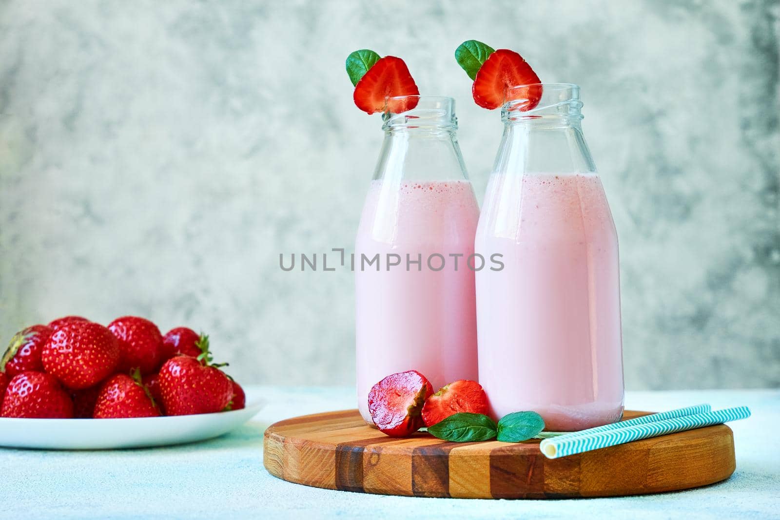 Close-up strawberry smoothie or milkshake in glass jar with berries on wooden board on blue concrete background. Healthy summer drink.