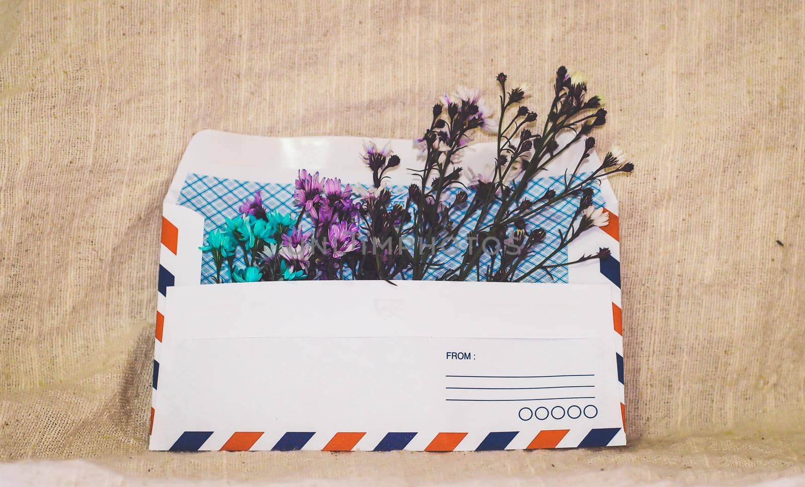 Opened envelope with small little flowers arrangements on linen background, top view. Festive greeting concept. by Petrichor