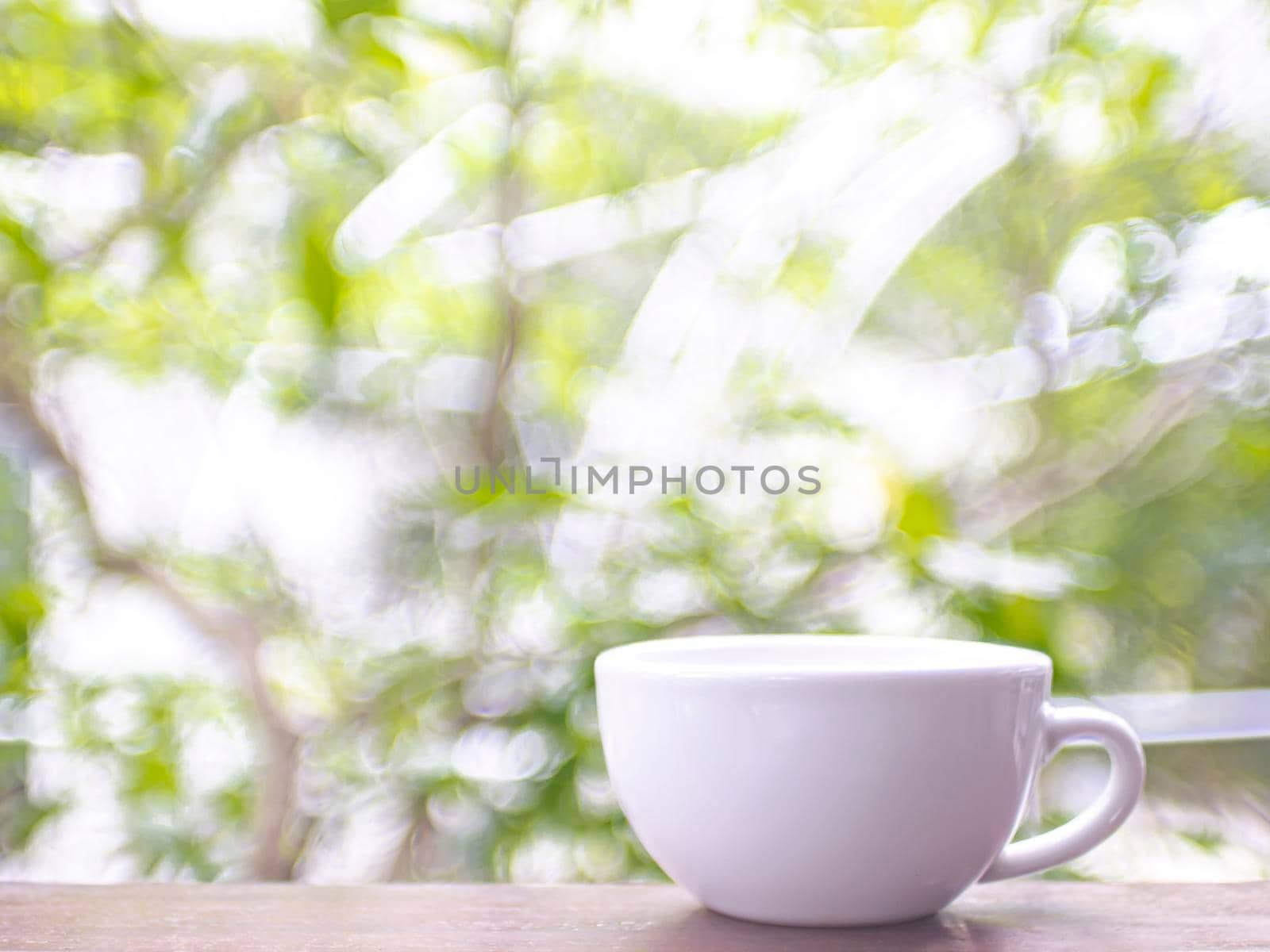 Blank White Mug Mockup on wooden table. Fresh Tree Branches with Green Leaves blur background