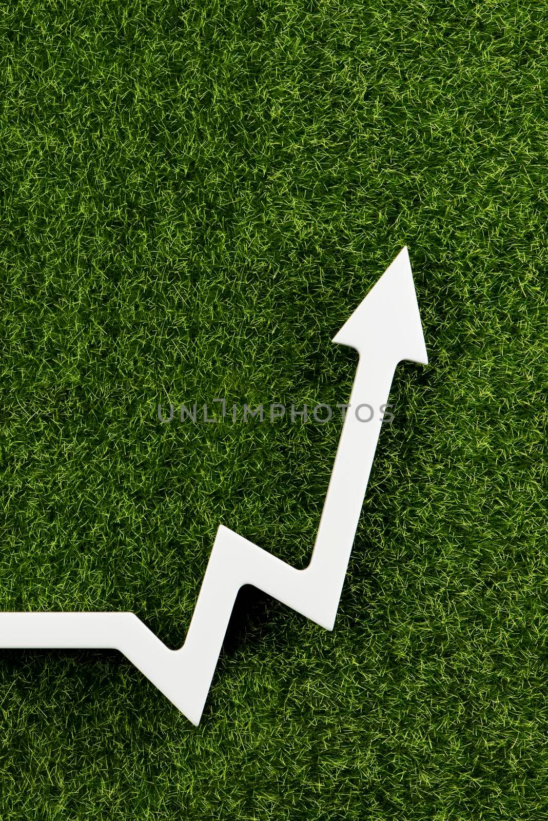 White chart arrow on green grass points up. Business development symbol, ecology concept, green energy
