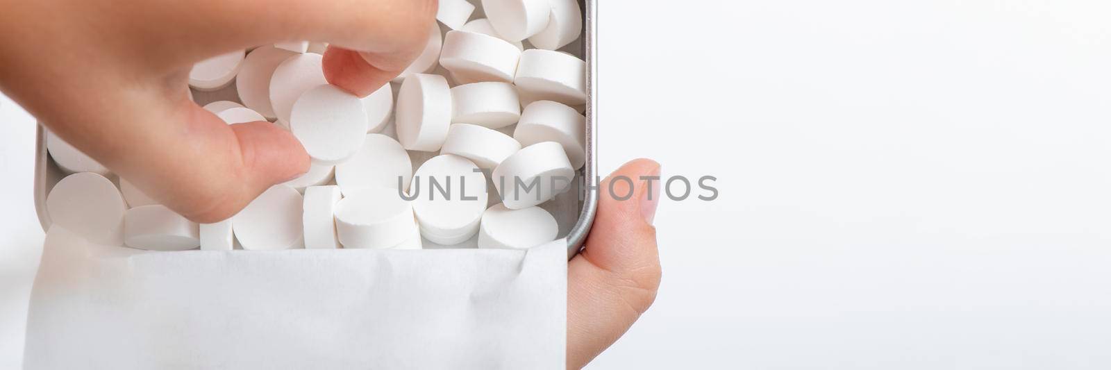 Mint candies on a white background. White mint candies in an open tin box. Fresh breath or bad breath concept. The child takes one lollipop out of the box with his hand. by SERSOL