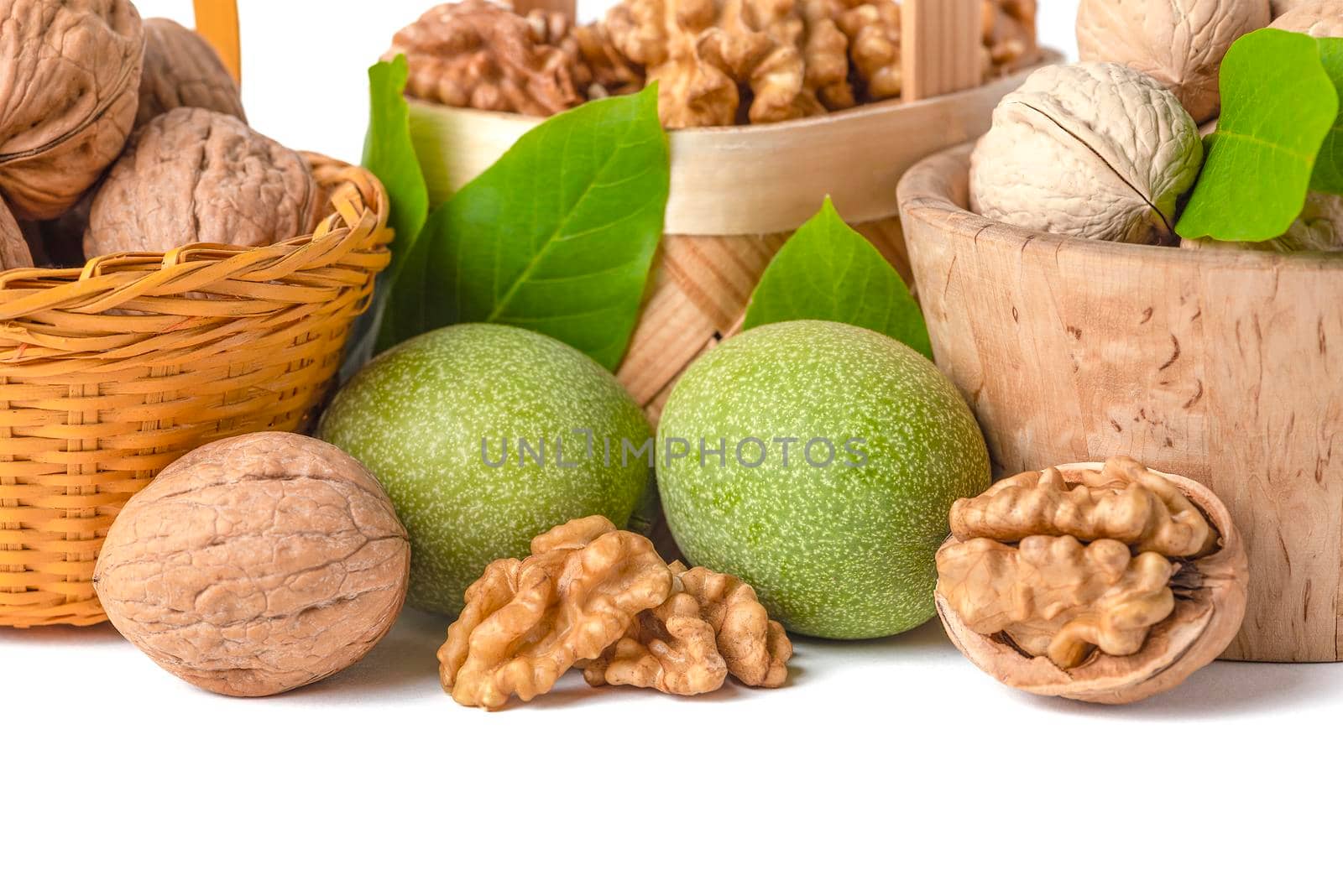 Walnut. Walnut fruits of different varieties lie in wooden saucers and baskets on a white isolated background. Nearby are green leaves and unripe walnut fruits