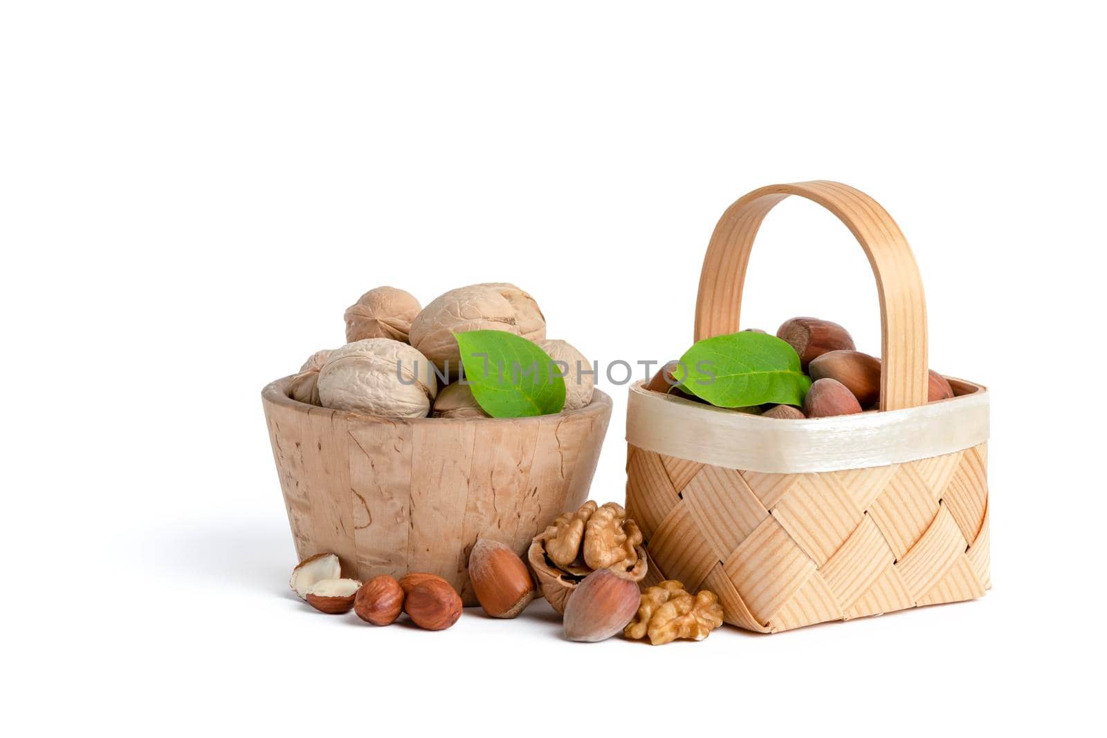 Walnuts and hazelnuts of different varieties lie in wooden saucers and baskets on a white isolated background. Nearby green leaves, walnuts and shelled hazelnuts.
