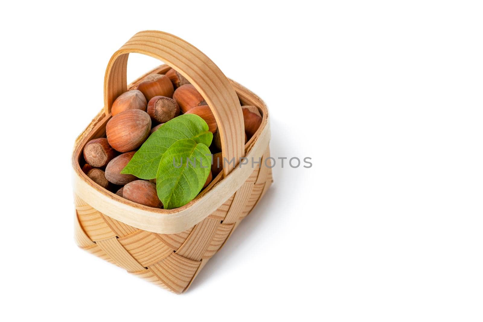 Hazelnut lies in a wooden basket on a white isolated background. Unpeeled hazelnuts in shell and green leaves.