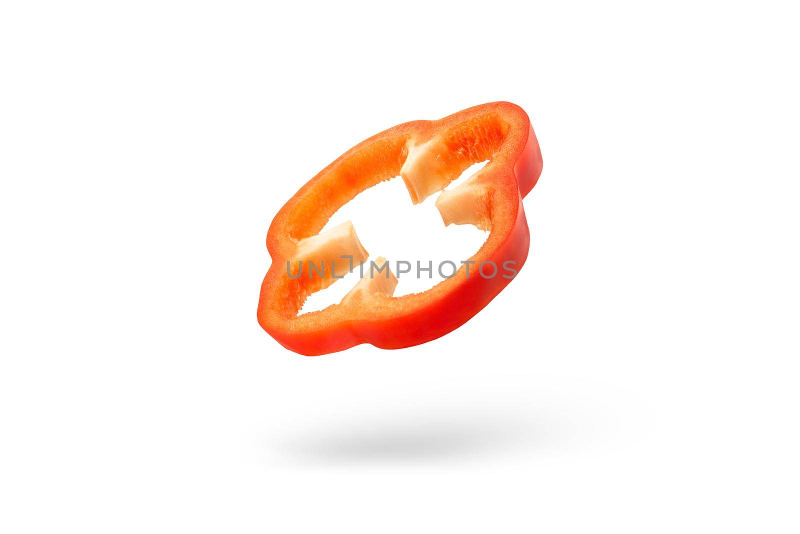 A slice of red paprika falls on a white backdrop. Red bell pepper flying in air on isolated white background.